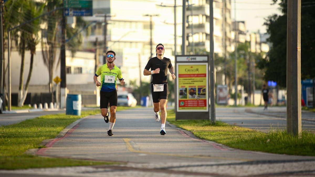 Two men jogging on an urban path, wearing sportswear during a sunny day run.